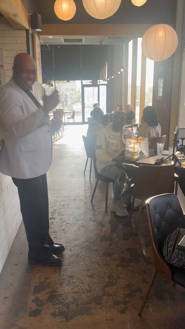 A host in a white blazer standing by tall downtown windows in the warm, candlelit dining room of The Flavor House