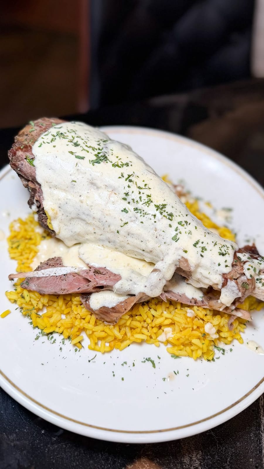 A hearty plate of sliced, seasoned meat fanned over golden Caribbean rice, finished with a parmesan cream sauce