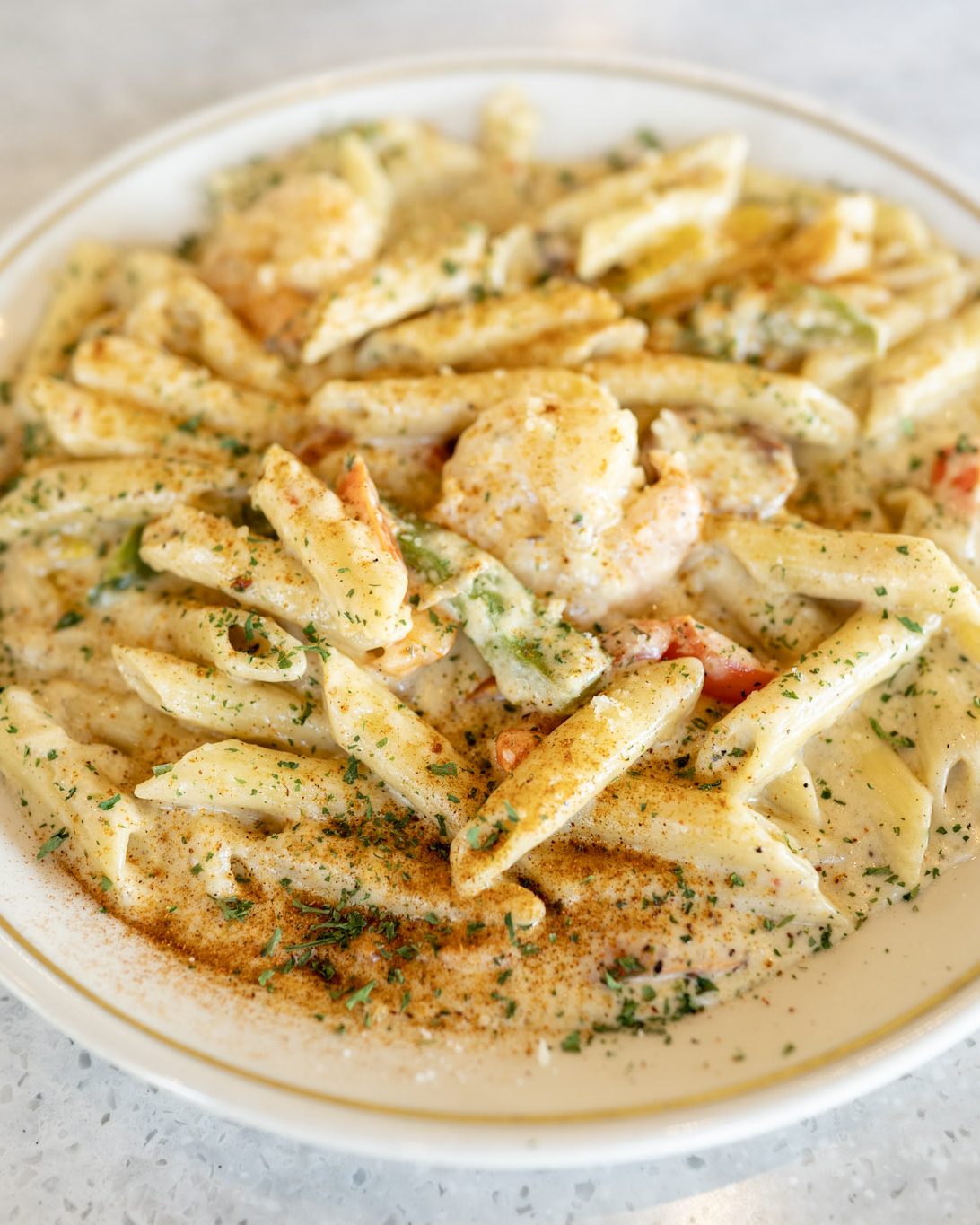 Rasta Pasta: penne and shrimp in a seasoned parmesan cream sauce with diced tomato and parsley, on a gold-rimmed plate on the marble bar
